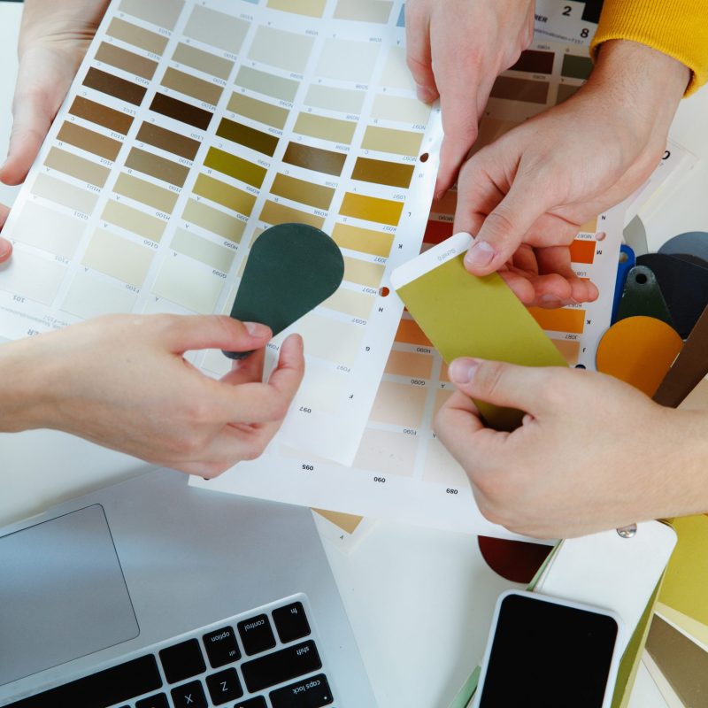 Interior designer working with young couple. Lovely family and professional designer or architector discussing conept of future interior, working with colour palette, room drawings in modern office.